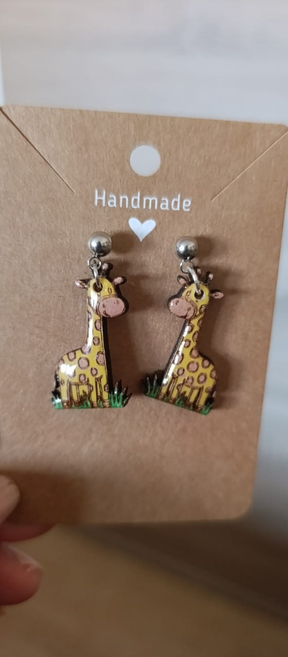 Pendientes de jirafa en color amarillo con detalles pintados a mano sobre fondo marrón claro.