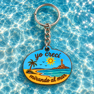 Llavero de madera con la frase «yo crecí mirando al mar» y paisaje costero sobre fondo azul con reflejos.